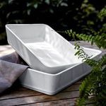 Two white rectangular stoneware bakers stacked outdoors on wooden surface with fern leaves and gray cloth