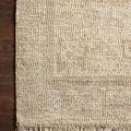 Ivory hand-woven rug with tonal textured pattern and fringed edges on a dark wood floor