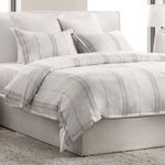 Angled view showing duvet's smooth drape over bed with multiple pillows in coordinating gray stripes