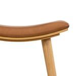 Close-up of curved padded butterscotch leather seat and natural wood grain on stool leg