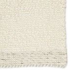 Close-up on rug surface highlighting thick, soft, looped cream wool texture with edge detail