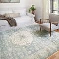 Rosette Denim Fog rug viewed at an angle in a bright living room with white sofa, gray chair, and wood floor