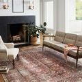 Rug styled in living room with fireplace, beige sofa, armchair, wood floors, and potted plant