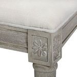 Close-up of hand-carved floral rosette detail on the stool's corner block under white upholstered seat