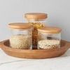 Three natural wood top canisters arranged on a round wooden tray from a slight angle