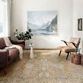 Rosemarie Gold/Sand rug styled on hardwood floor in a bright living room with leather and fabric seating
