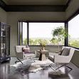 Black cabinet styled in modern living room corner with large windows and gray armchairs around a small table.