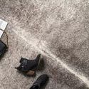 Close-up of the rug’s textured surface with black boots and a black purse on the grey and ivory rug