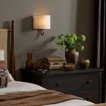 Sconce installed on wall above dark wood dresser with bedroom styling and green floral arrangement