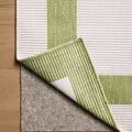 Corner of the rug lifted to display underside and attached felt furniture pad on wooden flooring.
