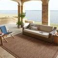 Rug styled in outdoor covered patio setting with wicker sofa and lake view background