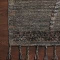 Corner of rug on dark wood floor highlighting fringe tassels and woven border