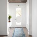 Light blue and ivory runner rug laid in a narrow modern hallway with hardwood floors and white walls
