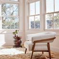 Inez Brown Pine End Table styled next to a white upholstered chair in a bright living room with large windows and a sheeps...