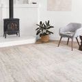 Lucia Mist Rug placed in a cozy room with white walls, a gray chair, black stove, and woven basket plant pot