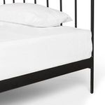 Close-up of black iron side frame and bedpost with white fitted sheet and pillow edge