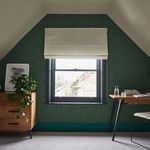 Teal grasscloth wallpaper applied on slanted wall surrounding a window in cozy room with wooden furniture