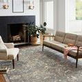 Rug styled in modern living room beneath mid-century sofa and armchair with fireplace and plants