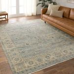 Rug styled on wood floor next to tan leather sofa with pillows in bright room