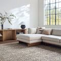 Woven rug styled under beige sectional sofa in bright room with large window and wooden beams