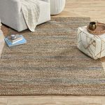 Rug styled in a living room setting with armchair, pouf, books, and wooden floor
