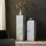 Styled interior scene with two varying height marble pedestals against dark wall and wooden floor