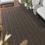 Rug styled outdoors on wooden deck partially under white sofa and chair, with plants nearby