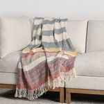 Throw blanket draped casually over corner of cream sofa showcasing full stripe pattern and fringe detail