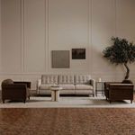 Living room scene with sofa in upright position between two brown armchairs and wall artwork