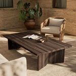 Joette Outdoor Coffee Table shown in an outdoor seating area with woven armchair and textured rug
