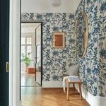 Room view with Esther Wallpaper covering walls, decorated with a bench, round mirror, and framed print on wood floor