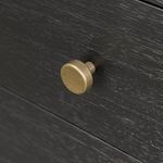 Extreme close-up of a single brass-finished round drawer knob with textured black wood background