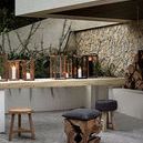 Outdoor setting with multiple lit storm lanterns placed on stone table, surrounded by stone and wood stools