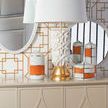 Tobago mirror reflecting white and gold textured lamp with orange and white jars on beige cabinet with geometric wallpaper