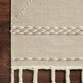 Corner detail of Sawyer Sand Rug with chunky braided weave border and tasseled fringe on wood floor