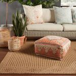 Indoor corner view featuring rug topped with orange patterned pouf and rattan lanterns