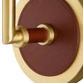Detailed close-up of stitched tan leather wrapped around circular wall plate and gold arm base