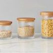 Set of three clear glass canisters with natural wood airtight lids, varying in size, containing dry food items
