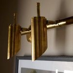 Close-up angled view of double sconce highlighting the aged patina brass finish and mounting above artwork
