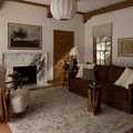 Milena Sage rug styled in a living room with brown sofa, armchair, wooden beams, and marble fireplace