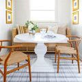 Rug styled under dining table with wicker bench and wooden chairs in light bright room