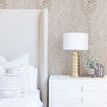 Shagreen wallpaper applied on bedroom wall with white upholstered bed and gold lamp on white bedside table