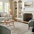 Delfin End Table placed next to a green armchair in a bright living room with fireplace and large windows