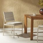 Side angle showing chair positioned next to wood outdoor dining table in sunlit patio setting