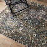 Close shot of rug corner beneath black rocking chair showing faded blue and gold pattern on wood floor