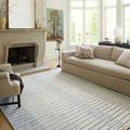 Rug in living room setting with beige sofa, armchair, fireplace, and large windows illuminating striped pattern