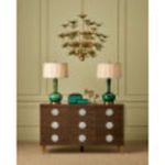 Blurry interior dining space with chandelier above wooden sideboard and green lamps