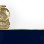 Close-up of textured gold trim and circular hanger against navy enamel on wall frame