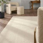 Living room scene with rug framed by boucle chair, ottoman, and wooden desk against white walls
