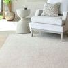 Light beige rug styled in a bright room under a light gray armchair with textured beige pillow and concrete side table